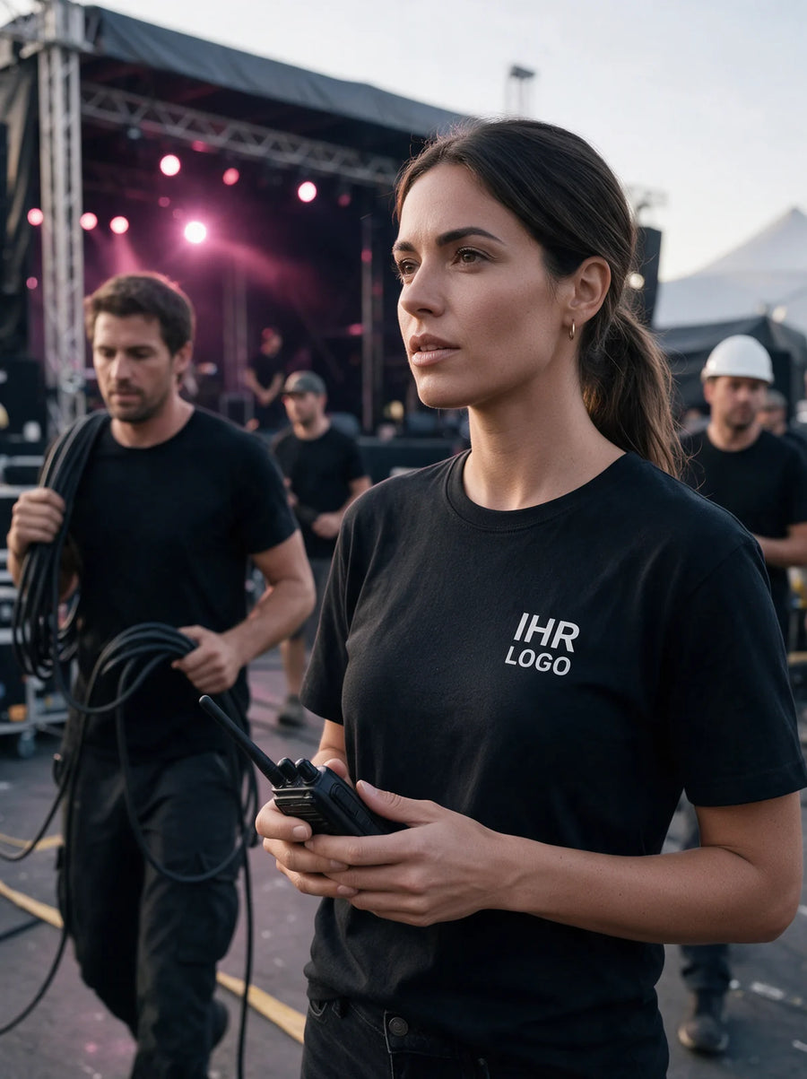 Eventteam in schwarzen T-Shirts mit weißem Brustlogo beim Aufbau vor einer Festivalbühne.