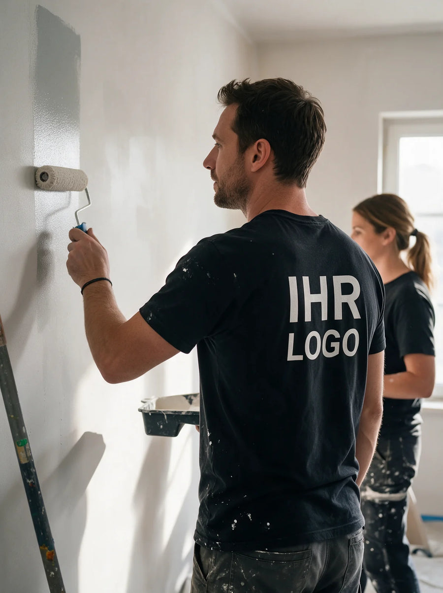 Maler in schwarzem T-Shirt mit großem Rückenaufdruck beim Streichen einer Innenwand.