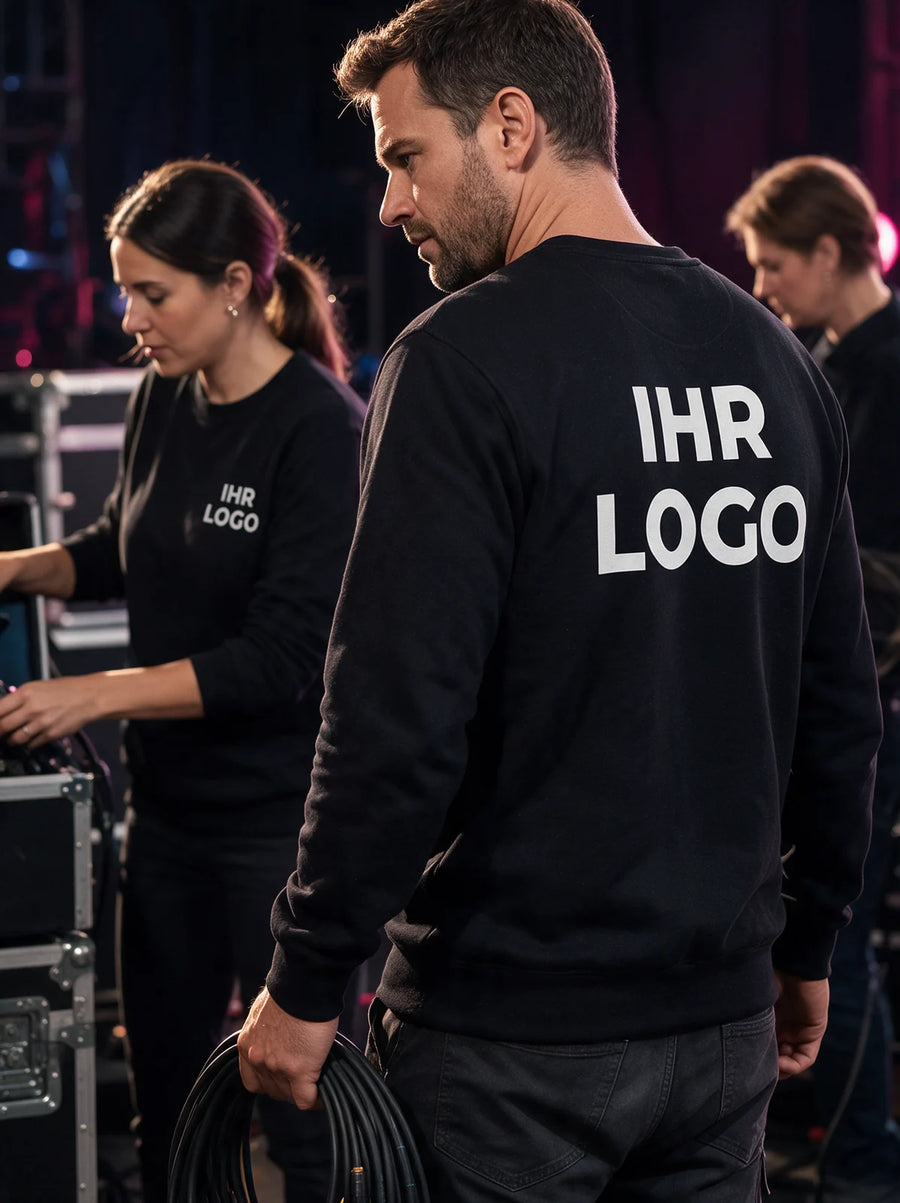 Bühnencrew in schwarzen Sweatshirts mit Brust- und Rückenaufdruck vor beleuchteter Veranstaltungstechnik.
