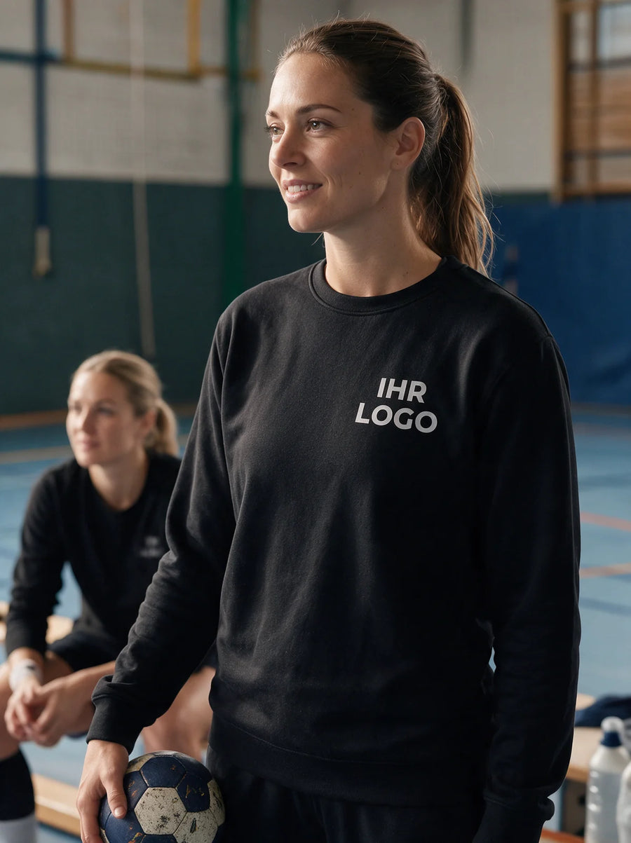 Handballspielerinnen in schwarzen Rundhals-Sweatshirts mit weißem Brustlogo in der Sporthalle.